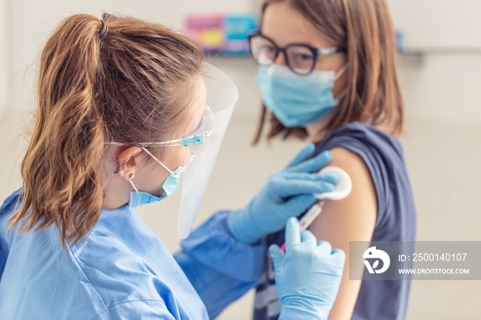 Female halthcare employee applies vaccine from injection into the arm of a young girl