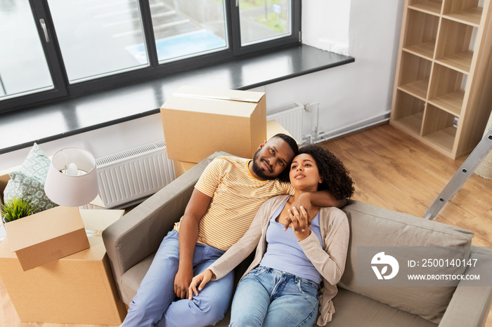 moving, repair and real estate concept - happy african american couple with cardboard boxes sitting on sofa at new home