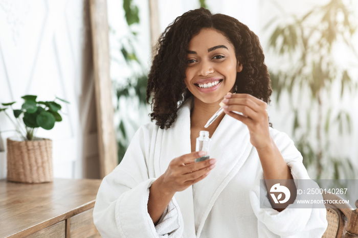 Afro Woman In Bathrobe Holding Organic Serum, Ready To Apply On Face