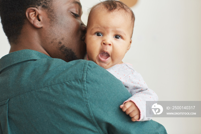 Back view portrait of young African-American father holding son with cute baby looking at camera over mans shoulder, copy space