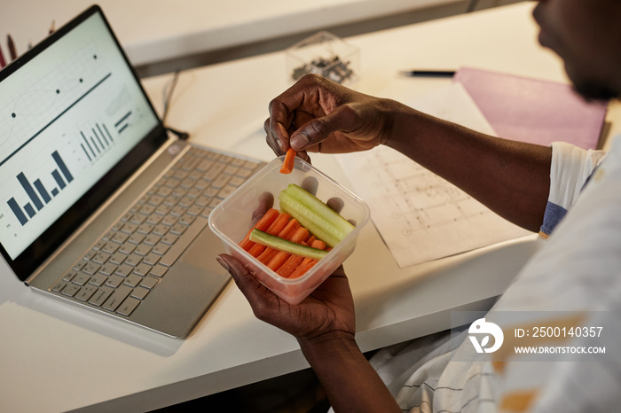 High angle closeup of young African American man eating healthy snack while working or studying late at night, copy space