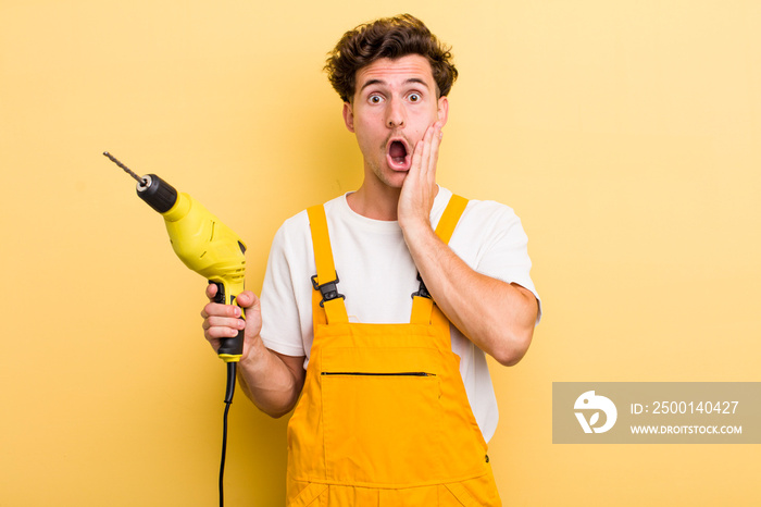 young handsome guy feeling shocked and scared. handyman with a drill concept