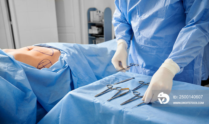 Surgeon in sterile gloves getting ready medical instruments. Patient with marks on skin lying on bed while doctor preparing scissors, forceps and scalpels. Concept of plastic surgery preparation.