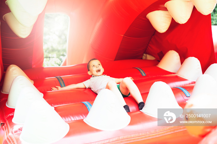 Little boy child lies on a toothy inflatable mouth of a multi-colored slide