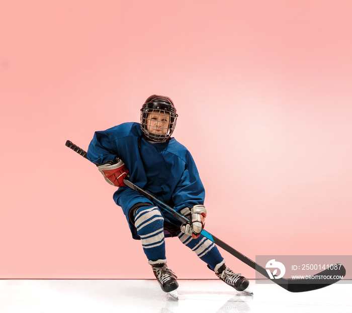 A hockey player in uniform with equipment over pink studio background. The athlete, child, sport, action concept