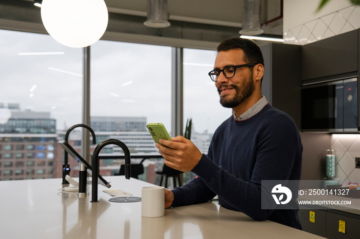 Man using smart phone in office kitchen