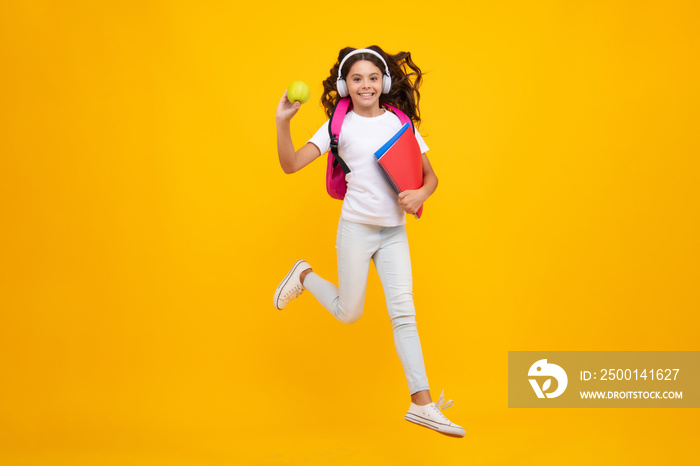 Schoolgirl, teenage student lifestyle girl in headphones hold books on yellow isolated studio background. School and music education concept.