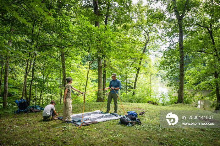 Air Force service member sets up a tent with his sons on  a backpacking trip.