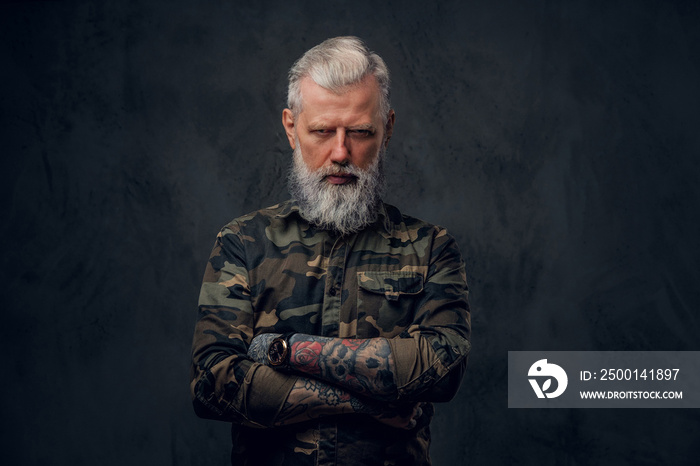 Brutal martial grandfather dressed in military clothing poses in dark background with crossed arms.