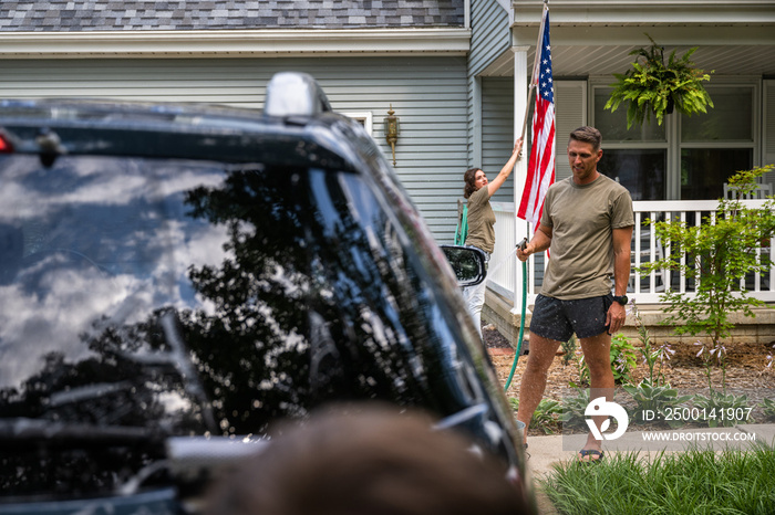 Air Force service member washes his vehicles with his sons in the driveway.