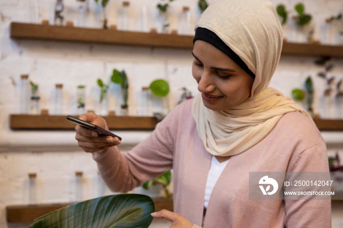 Woman wearing headscarf photographing banana leaf with smart phone