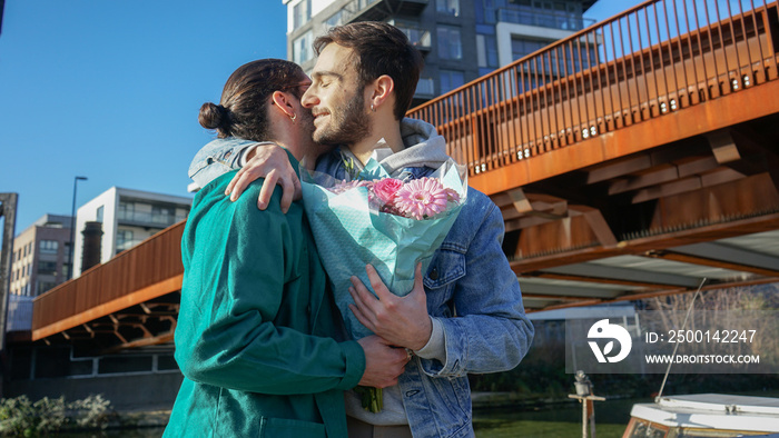 Smiling gay couple with bouquet embracing outdoors