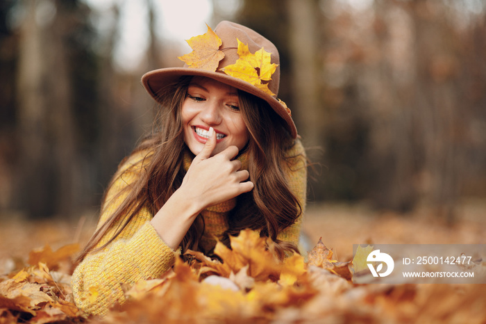 Young woman model lying in autumn park with yellow foliage maple leaves. Fall season fashion