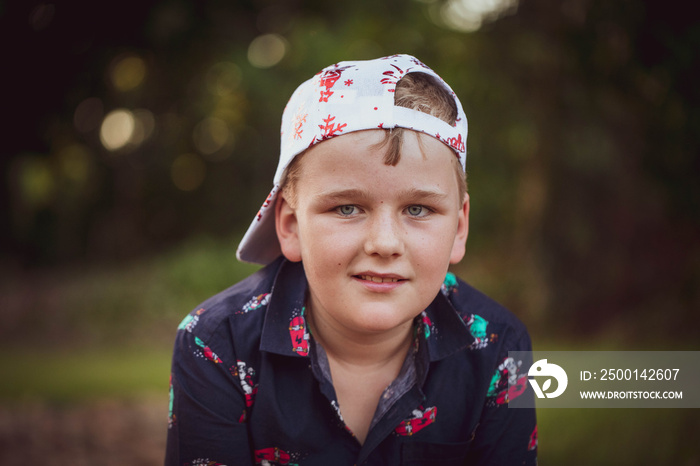 Pre-teen boy in Christmas outfit sitting in a relaxed style with hat backwards