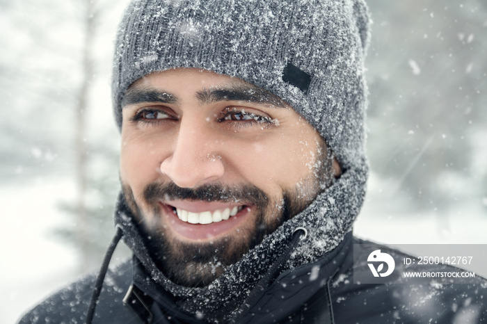 Happy bearded Middle eastern man wearing winter clothes under the snow