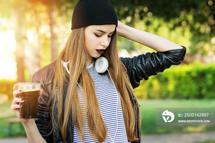 Cool young woman with dark lipstick, beanie and glass of dark beer in park