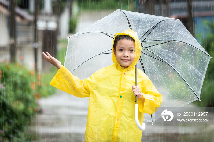 Asian kid holding an umbrella and catching raindrops. Happy Asian little child boy having fun playing with the rain in the evening sunlight.