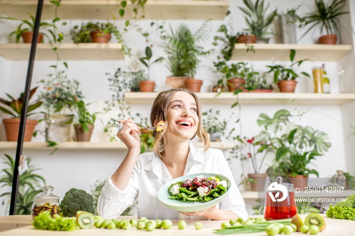 Young woman eating healthy food sitting in the beautiful interior with green flowers on the background