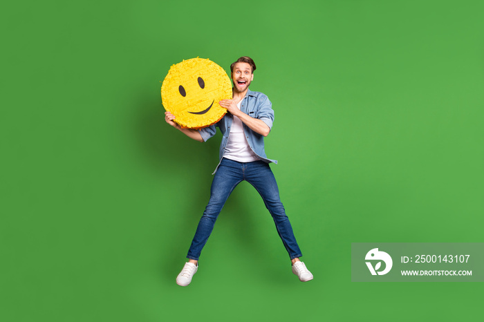 Full length body size photo of cheerful guy jumping high with yellow smile sign isolated vivid green color background