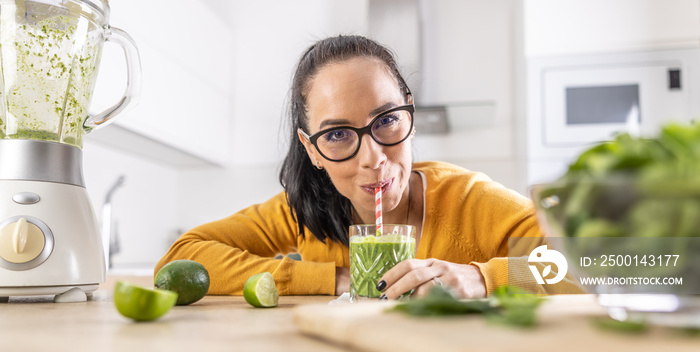 A funny young woman drinks a green smoothie that she made herself.