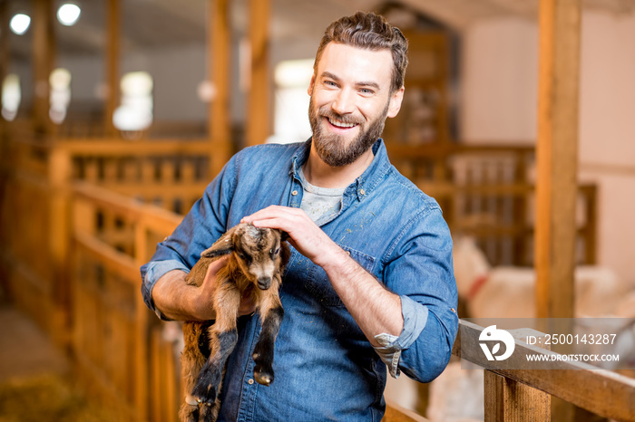 Handsome farmer taking care of cute goat baby at the barn