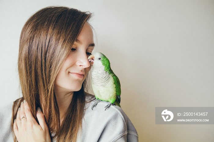 Cute green domesticated parrot snuggling on the shoulder of the owner feeling warm, comfortable and likes cuddling and  kissing. Monk Parakeet. Natural light photo