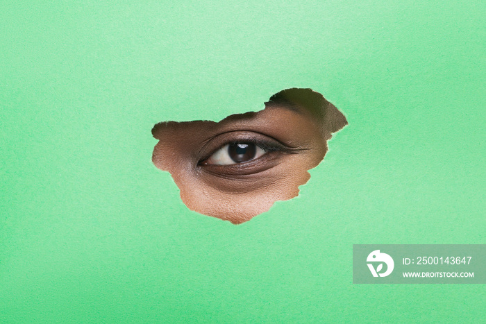 Black Woman’s Eye Without Mascara Looking Through Torn Green Paper