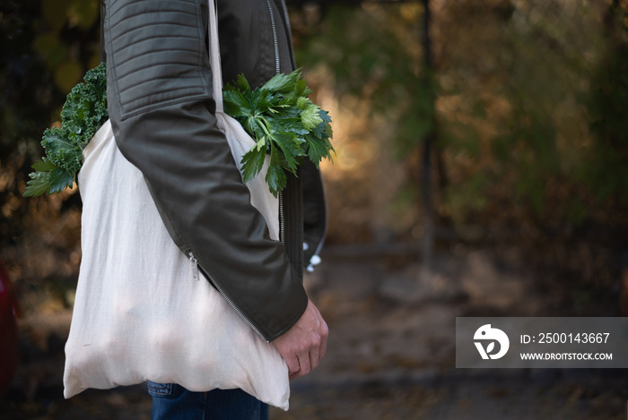 Young man holding reusable textile grocery bag with green vegetables