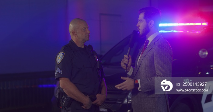 FIXED Reporter conducts interview with police representative on a crime scene. Police car lights flashing in the background. Model released for commercial use