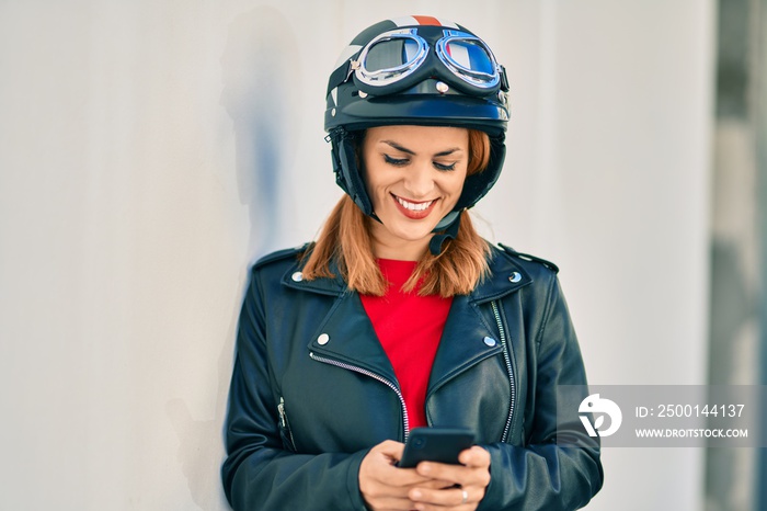 Young latin woman wearing motorcycle helmet using smartphone at the city.