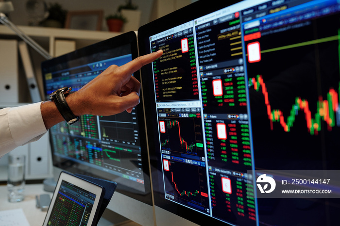 Close-up image of trader is pointing at graphs on computer screen and analyzing data and prices of assets