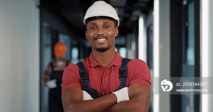 African american engineer in protective helmet and uniform posing confident for camera inside construction building interior. Architect concept.