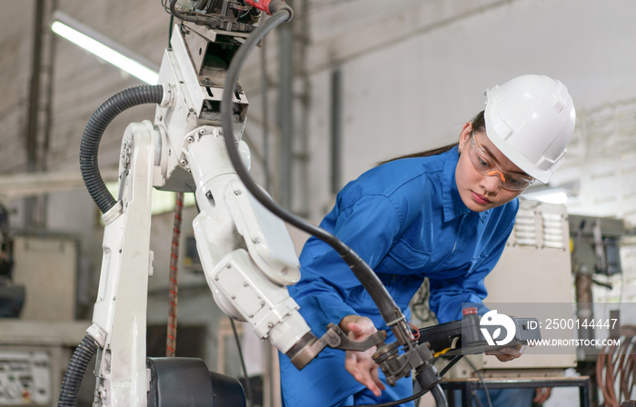 Female engineer checking robotic arm machine for system welding with remote control at a factory Industrial