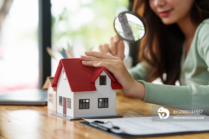 A woman holding magnifying glass and checking house model .Real Estate House Appraisal And Inspection concept.