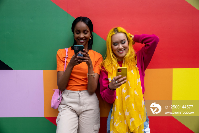 Young female friends using phones outdoors