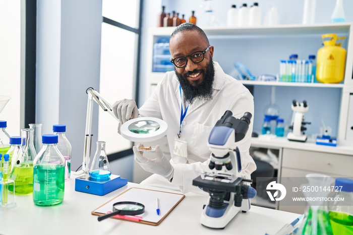 Young african american man wearing scientist uniform using loupe at laboratory