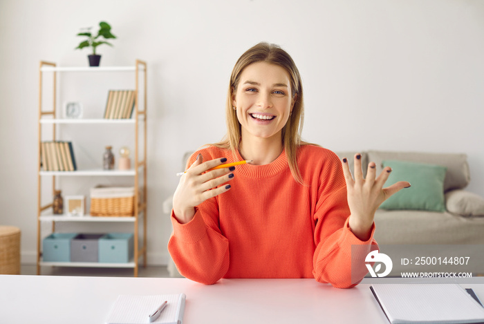 Positive woman talking and conducting online counseling or training while sitting in home office. Female online teacher, tutor or trainer having fun telling something while sitting in front of webcam.