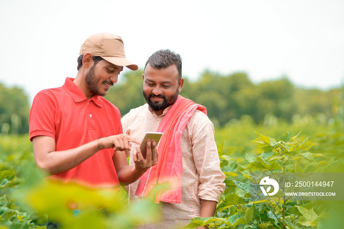 Young indian agronomist or banker showing some information to farmer in smartphone at agriculture field.