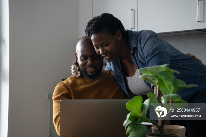 Man and pregnant woman looking at laptop in kitchen