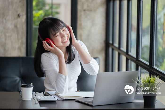 Happy woman is listening music via headset while working or study on laptop at home or office space.