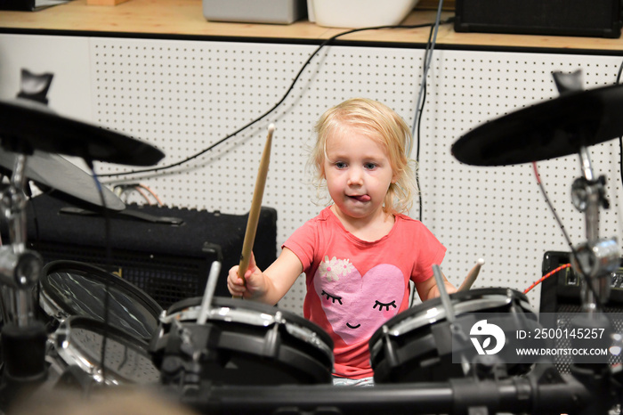 A little girl tries to play the drum kit at a music school.