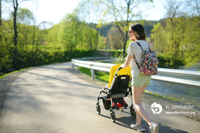 Teenage sister walking in a park with toddler brother in pushchair. Girl pushing a stroller for infant brother.