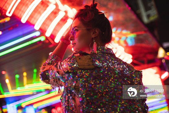 Stylish woman wearing jacket with shining sequins on the city street with neon lights