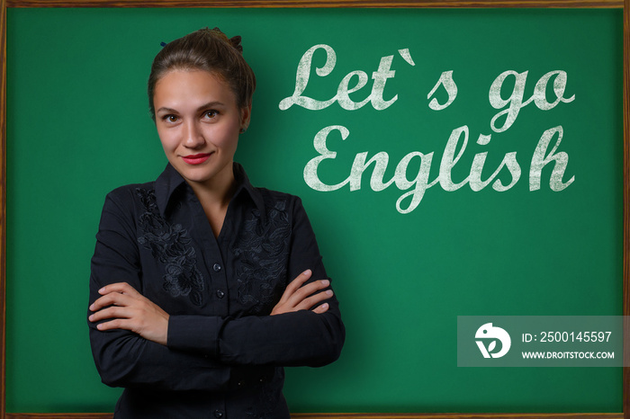 Beautiful young woman teacher (student, business woman) in classical dress standing near a blackboard with the inscription Lets go english