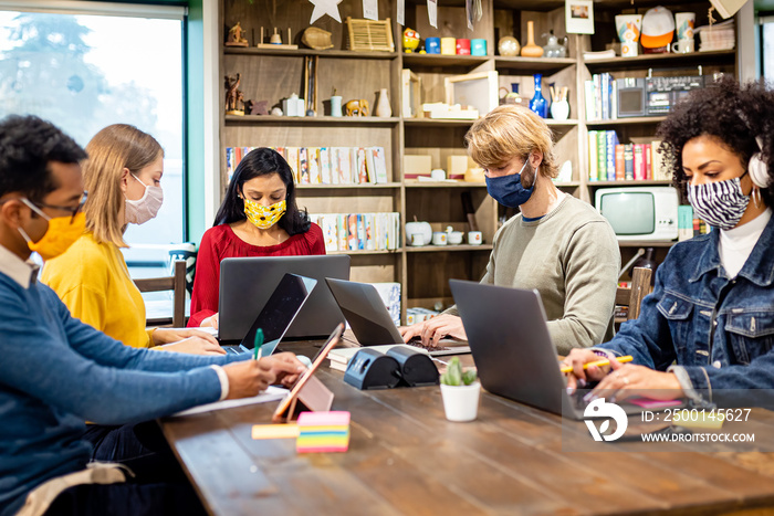 team of young millennials in a co-work space, group of students in the library studying during the coronavirus period, social distancing with protective masks, new normal, web connection and diversity