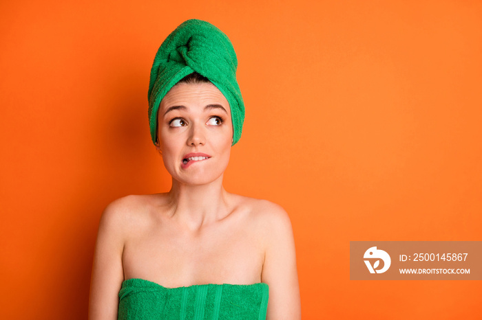 Photo portrait of scared woman in towels biting lip looking at blank space isolated on bright orange colored background