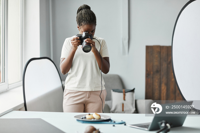 Minimal portrait of young African American woman taking food photography pictures in studio, copy space