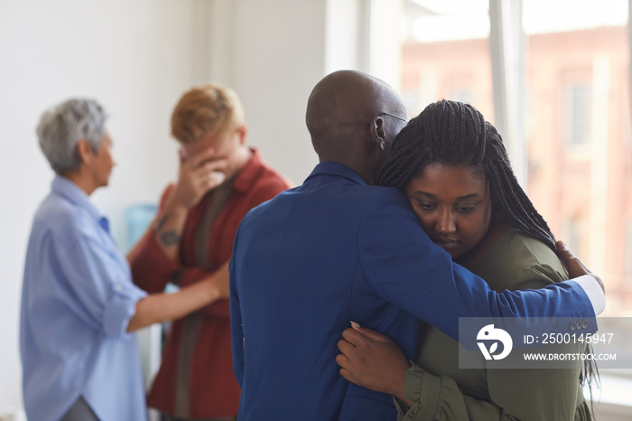 Waist up view at two African-American people embracing during support group meeting, helping each other with stress, anxiety and grief, copy space