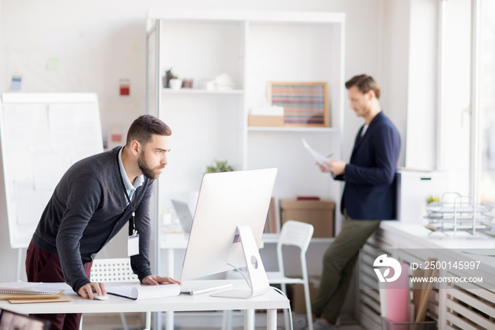 Side view portrait of bearded entrepreneur using computer standing at desk, copy space