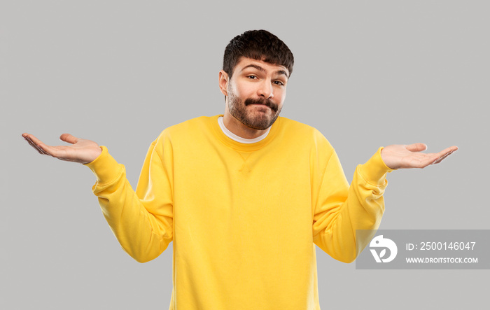 people, emotion and expression concept - confused man in yellow sweatshirt shrugging over grey background